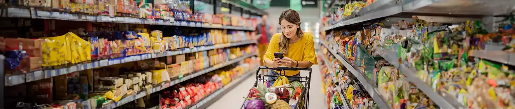 Cliente comprando con lista de verificación de teléfonos inteligentes, tomando productos del estante de la tienda.